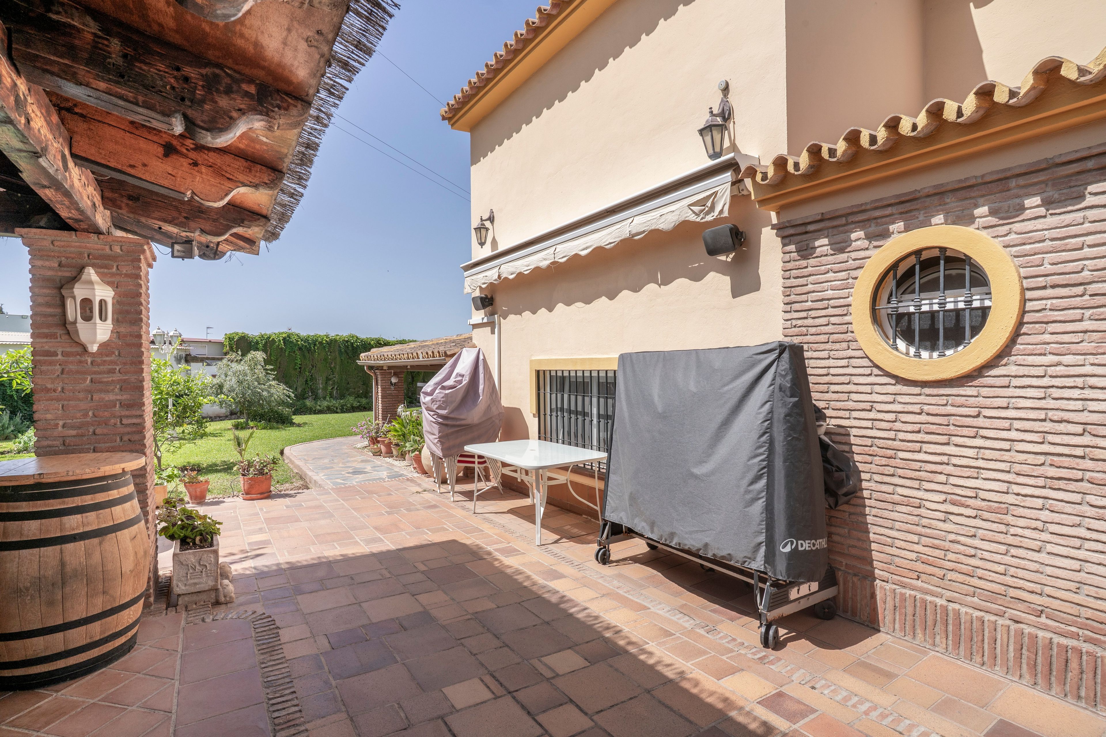 Un patio con mesa y sillas, una parrilla cubierta y un barril.