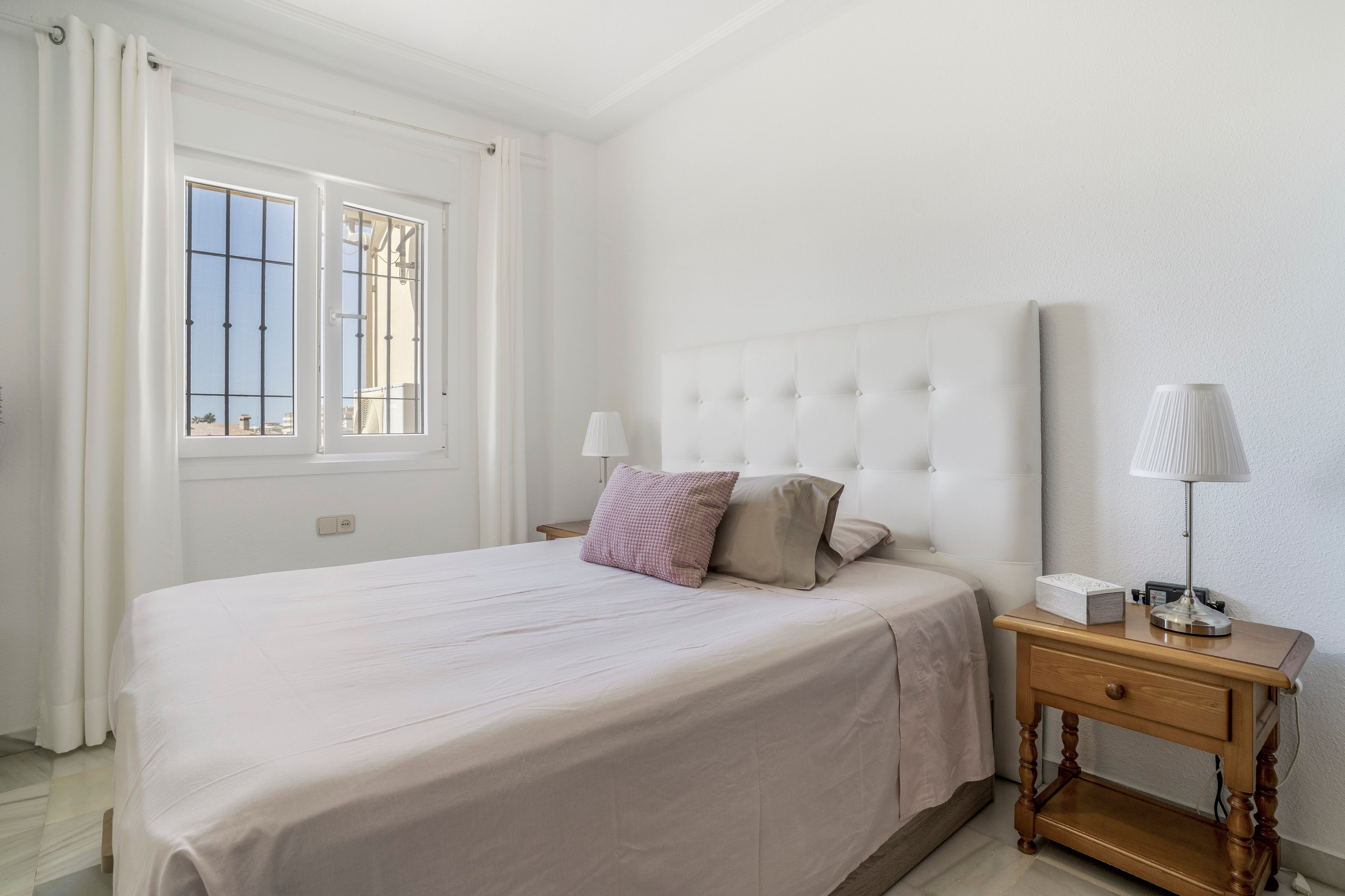 Un dormitorio con una cama, dos mesitas de noche, una ventana y una mesita auxiliar.