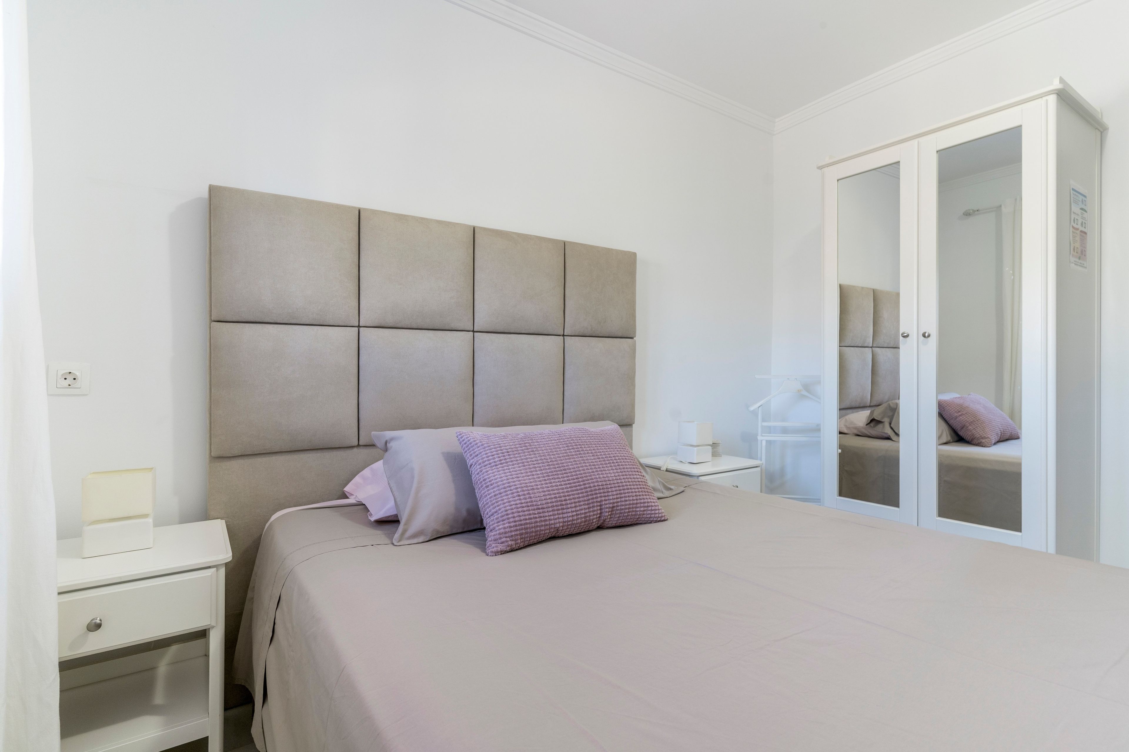 Une chambre à coucher comprenant un lit, des tables de chevet, une armoire et un miroir.