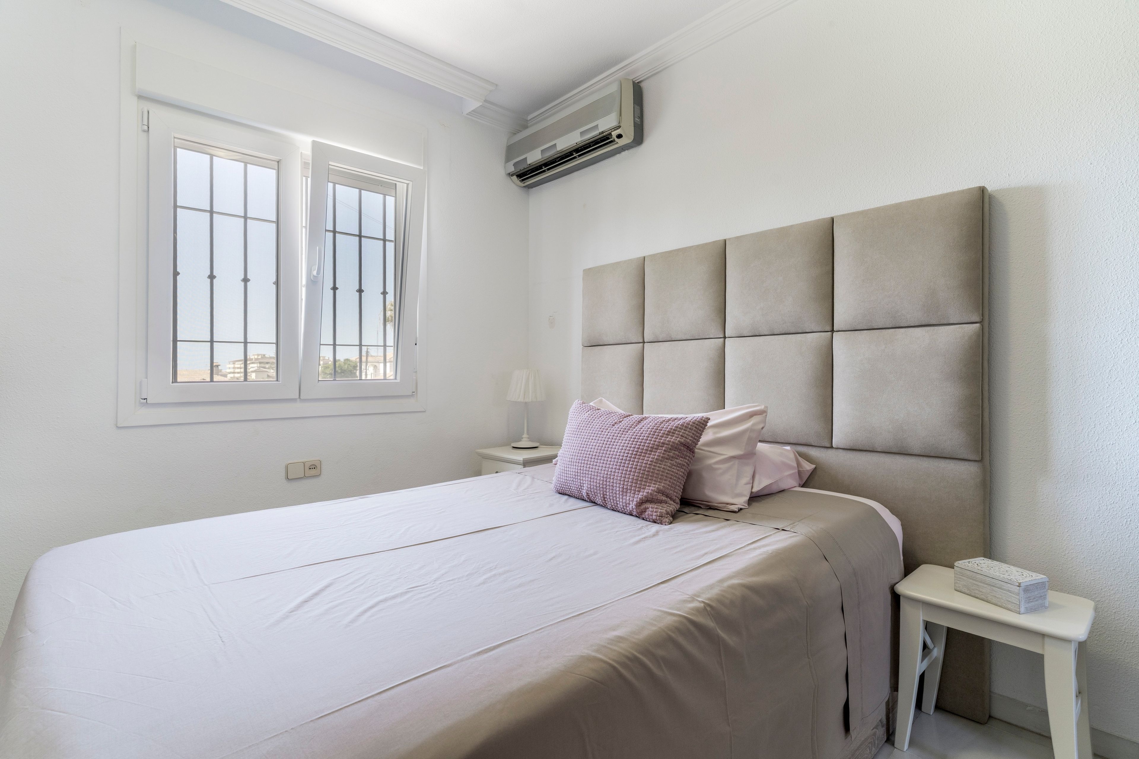 Een slaapkamer met een bed, nachtkastje, lamp, airconditioning en een raam.