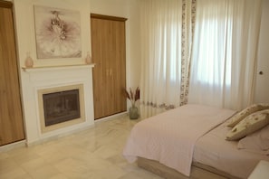 Un dormitorio con cama, chimenea y un amplio ventanal con cortinas.