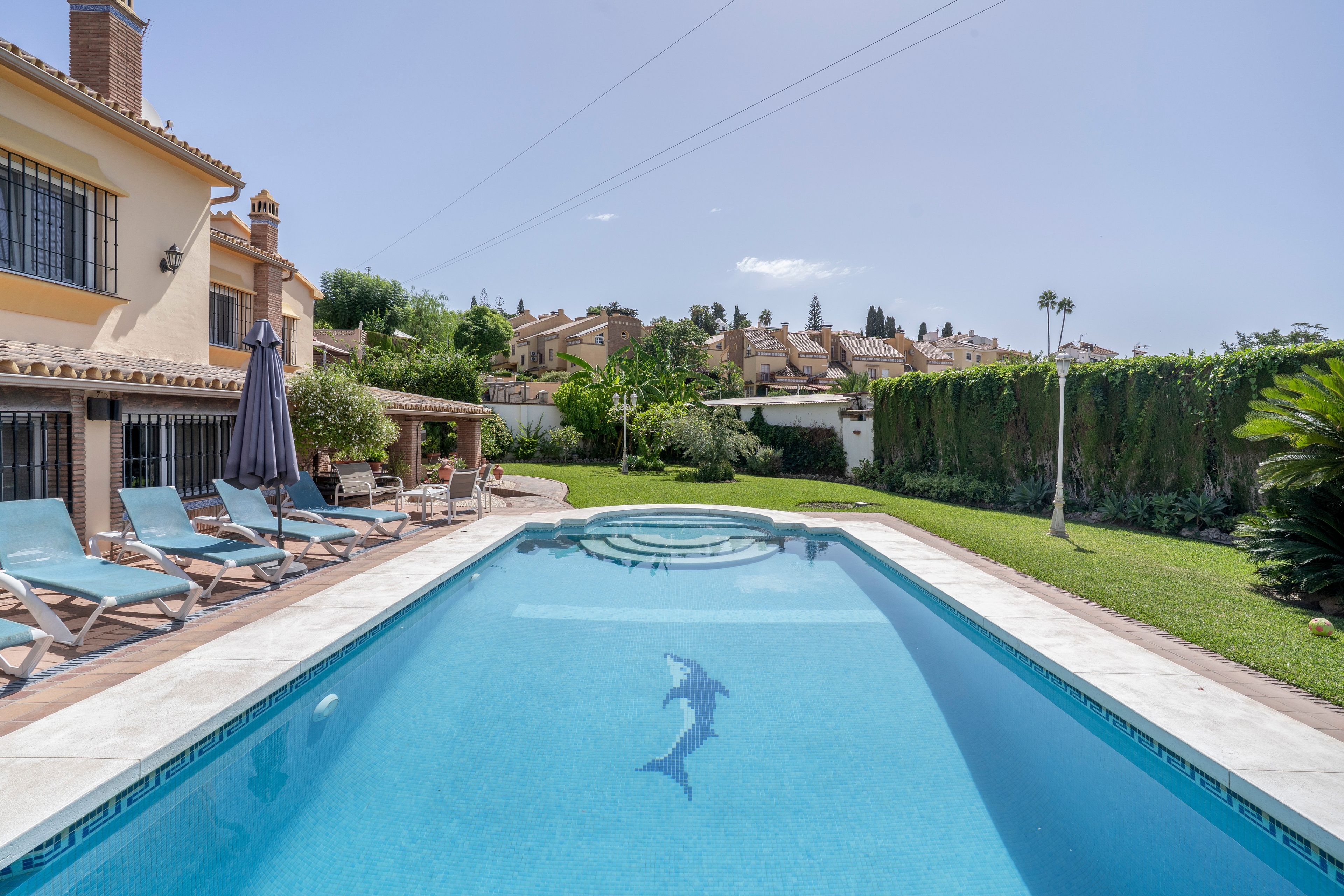 Una piscina con un diseño de delfín, rodeada de sillas de descanso y un césped bien cuidado.