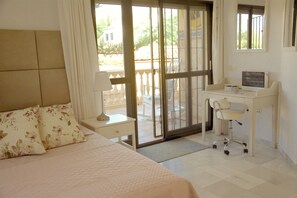 Quarto com cama, escrivaninha e vista através de uma porta de vidro.