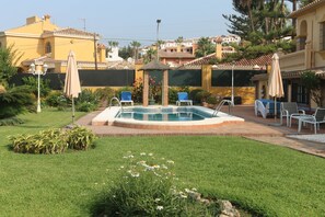 Ein Poolbereich mit Liegestühlen und Sonnenschirmen, umgeben von einer gepflegten Rasenfläche und einem Garten.