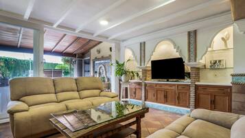 Amplia sala de estar con un sofá beige, una mesa de centro de vidrio y una cocina con armarios de madera y un televisor de pantalla plana.