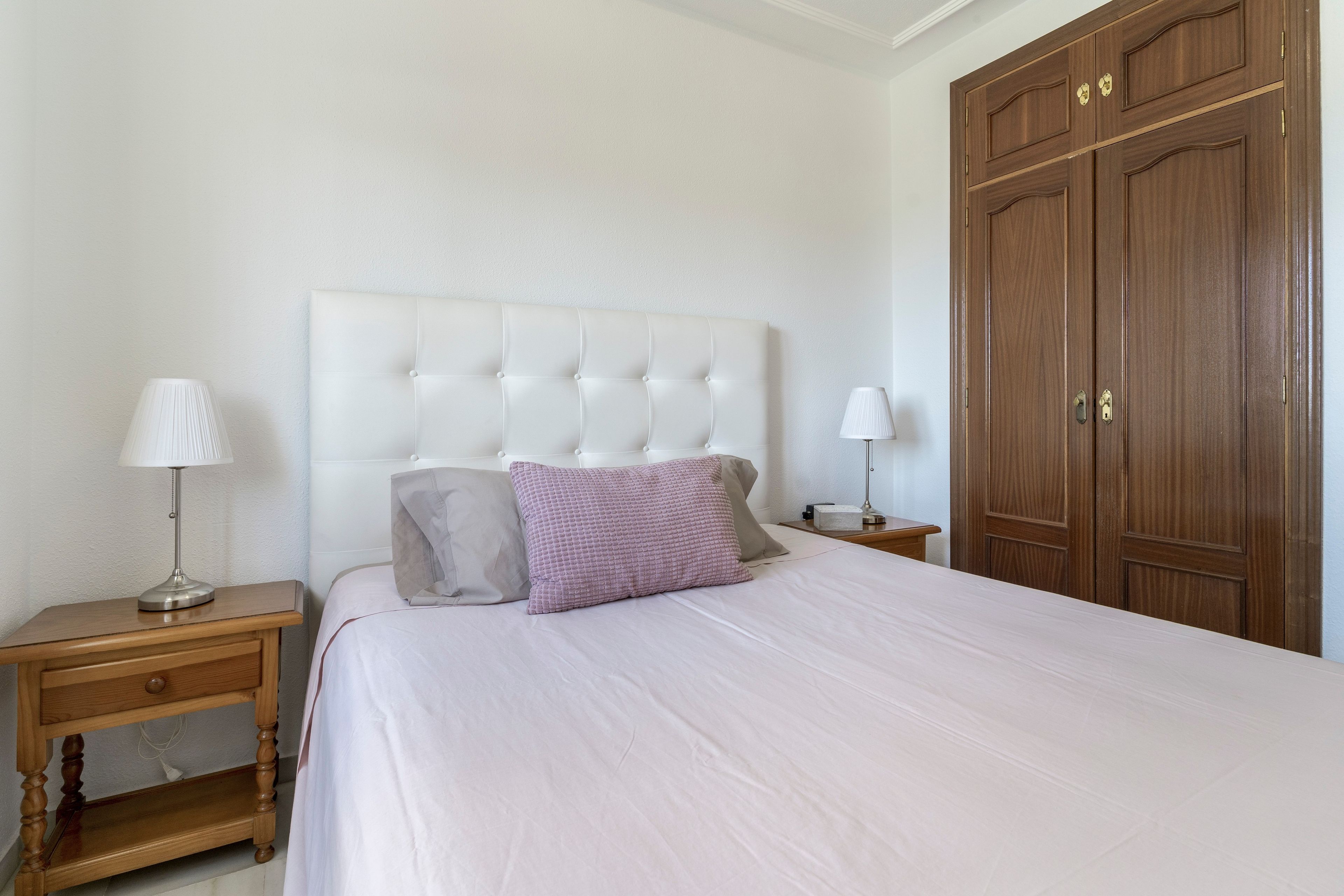 Een slaapkamer met een bed, twee nachtkastjes, een lamp, een kledingkast en een muur.