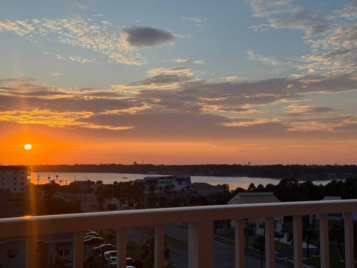 A sunset view from a balcony overlooking a body of water with buildings in the distance.
