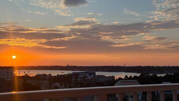 A sunset view from a balcony overlooking a body of water with buildings in the distance.