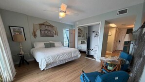 Een hotelkamer met een bed, een bureau, een stoel, een plafondventilator en uitzicht op de gang.