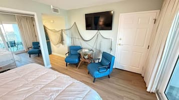 Une chambre d’hôtel avec un lit, deux chaises bleues, une petite table, un téléviseur et une porte.