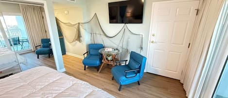 Una habitación de hotel con una cama, dos sillas azules, una mesita, un televisor y una puerta.