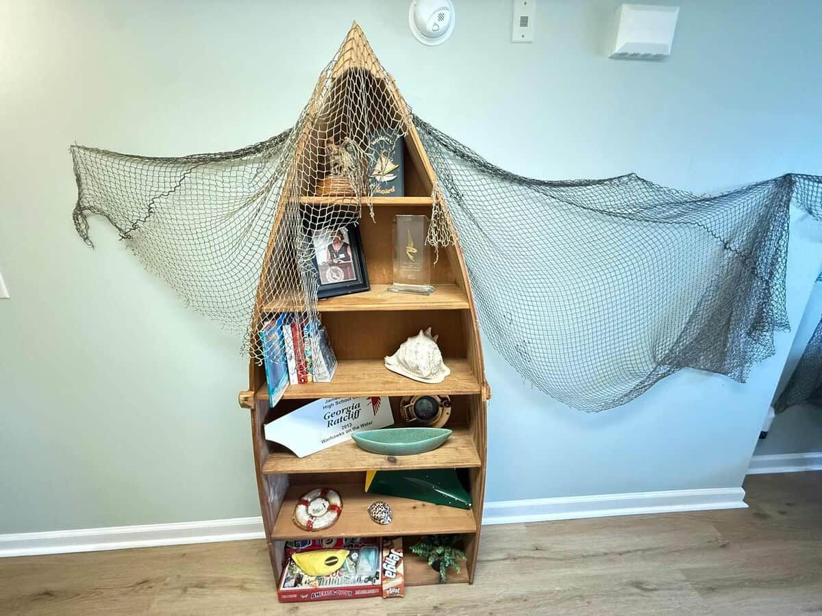 Ein Bücherregal mit einem Netzdach, Holzböden und verschiedenen Gegenständen, darunter Bücher und Dekorationsobjekte.