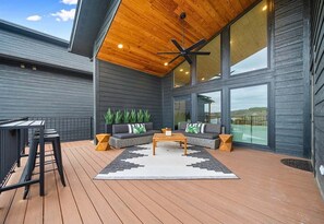 A covered outdoor seating area with a ceiling fan, a bar stool, a sofa, and a coffee table. - Private Pool, Dock, Movie Room on Lake Hamilton (Hot Springs)