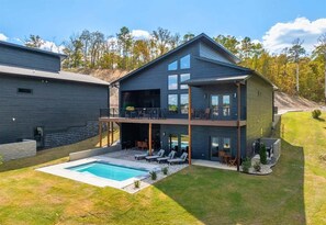 Ein modernes Haus mit zwei Etagen, einem Swimmingpool, einer überdachten Terrasse und Blick auf den umliegenden Wald.