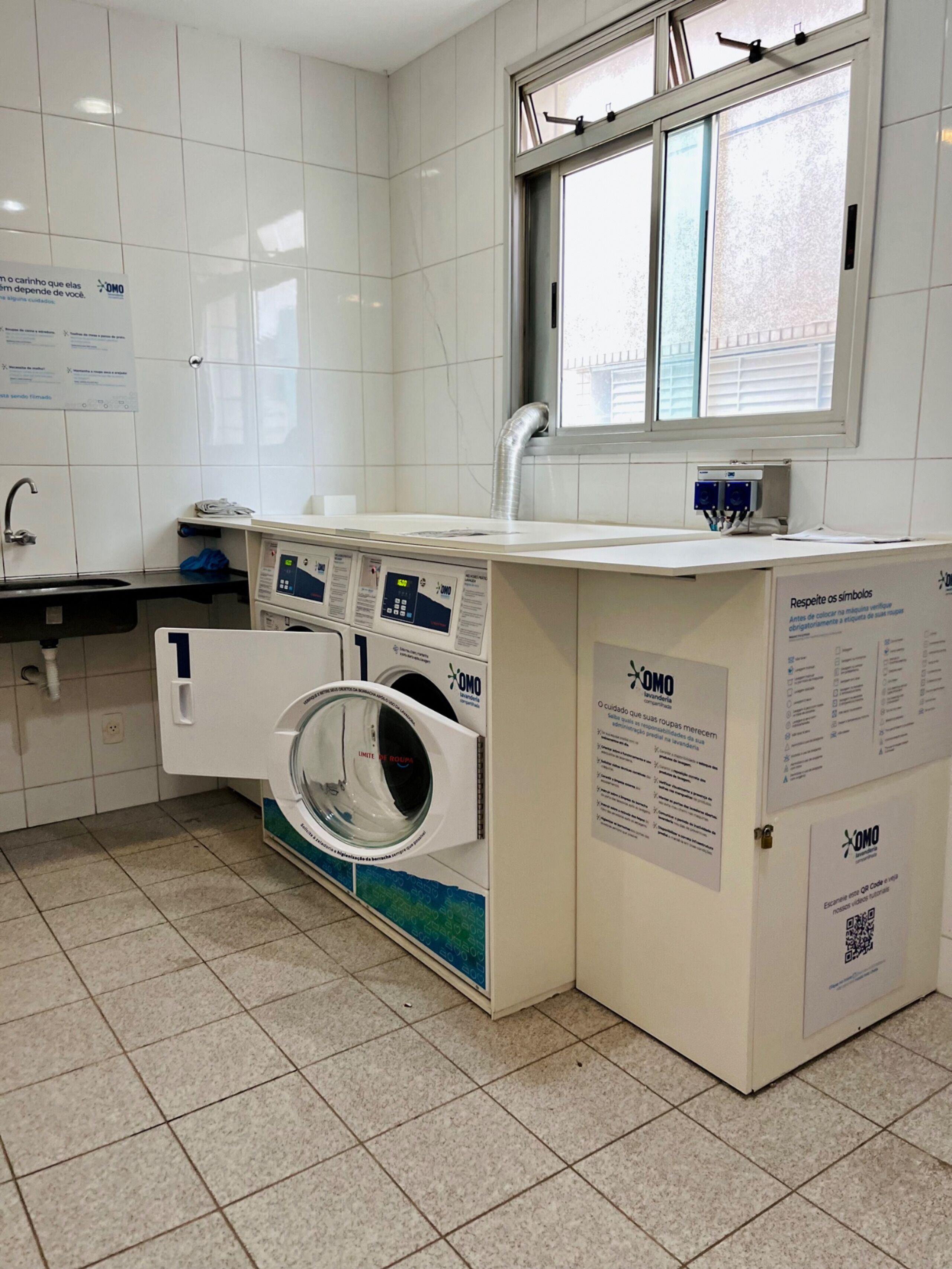 A laundry facility with a washing machine, a sink, and informational posters.