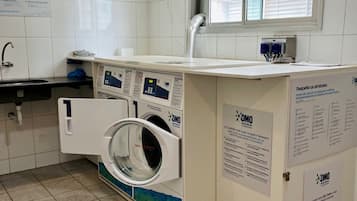 A laundry facility with a washing machine, a sink, and informational posters.