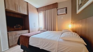 Un dormitorio con una cama, un aparador, un televisor y una ventana con cortinas.