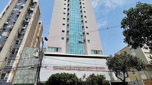 Un edificio alto con fachada central de vidrio azul, rodeado de otros edificios y un cielo despejado.