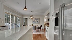A modern kitchen with a large island, stainless steel appliances, and a dining area with a view. - Central Royal Oak 3BR Home Near Woodward, Birmingham & Detroit Zoo (Royal Oak)