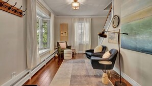 A room with a wooden floor, a large window with curtains, a round table, two armchairs, a floor lamp, and a painting on the wall. - Central Royal Oak 3BR Home Near Woodward, Birmingham & Detroit Zoo (Royal Oak)