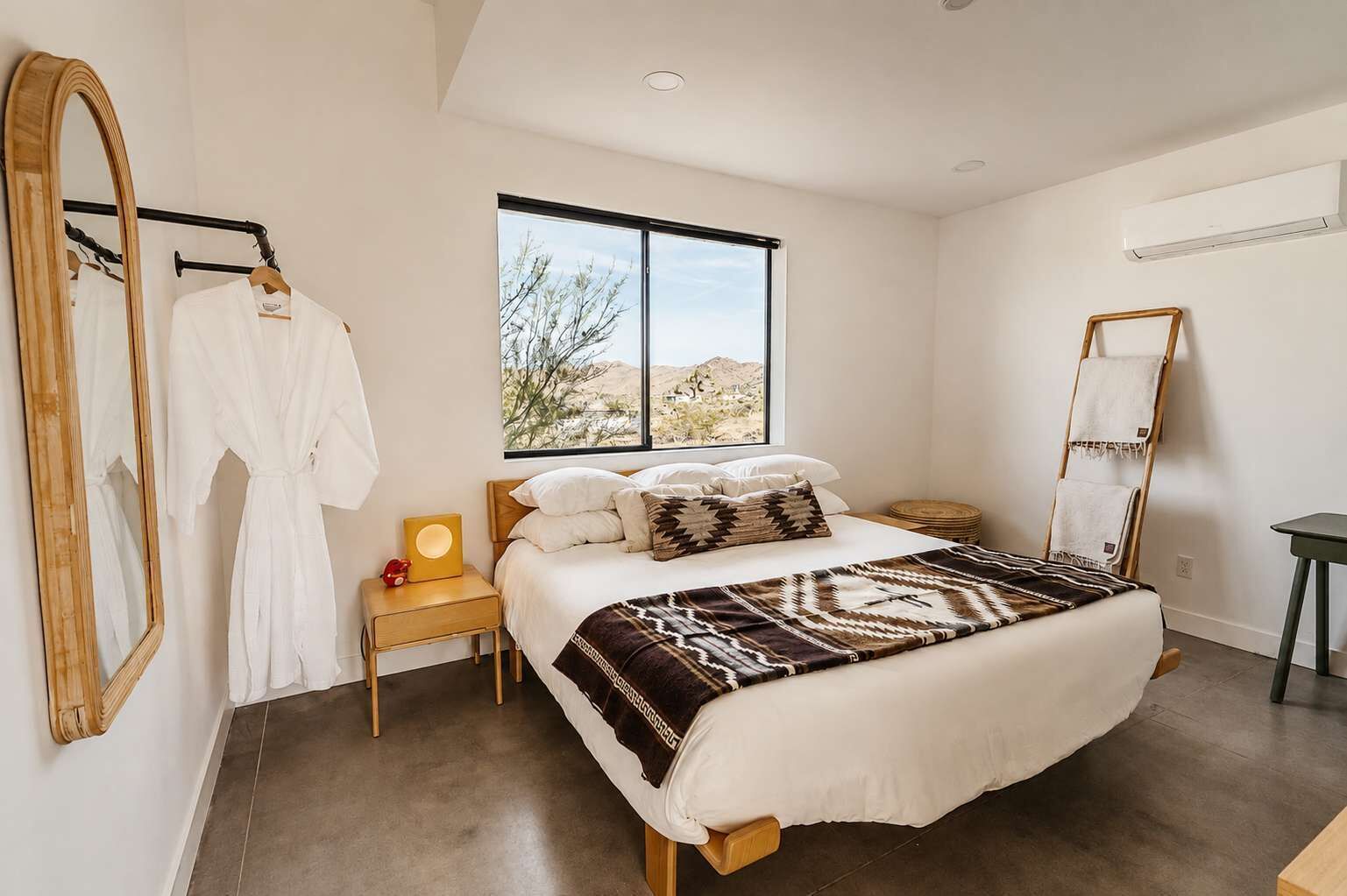Un dormitorio con una cama grande, una mesita de noche, un espejo y una ventana con vista al desierto.