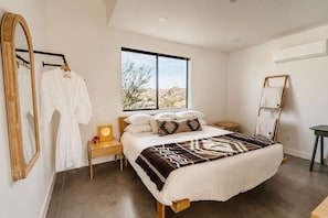 Un dormitorio con una cama grande, una mesita de noche, un espejo y una ventana con vista al desierto.