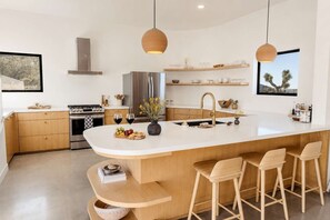 Una cocina moderna con una isla grande, taburetes de bar e iluminación colgante.