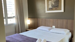 A hotel room with a large bed, a framed artwork on the wall, a window with curtains, and a bedside lamp. - LK Barro Preto 5 (Belo Horizonte)