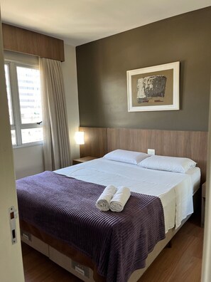 A hotel room with a large bed, a framed artwork on the wall, a window with curtains, and a bedside lamp. - LK Barro Preto 5 (Belo Horizonte)