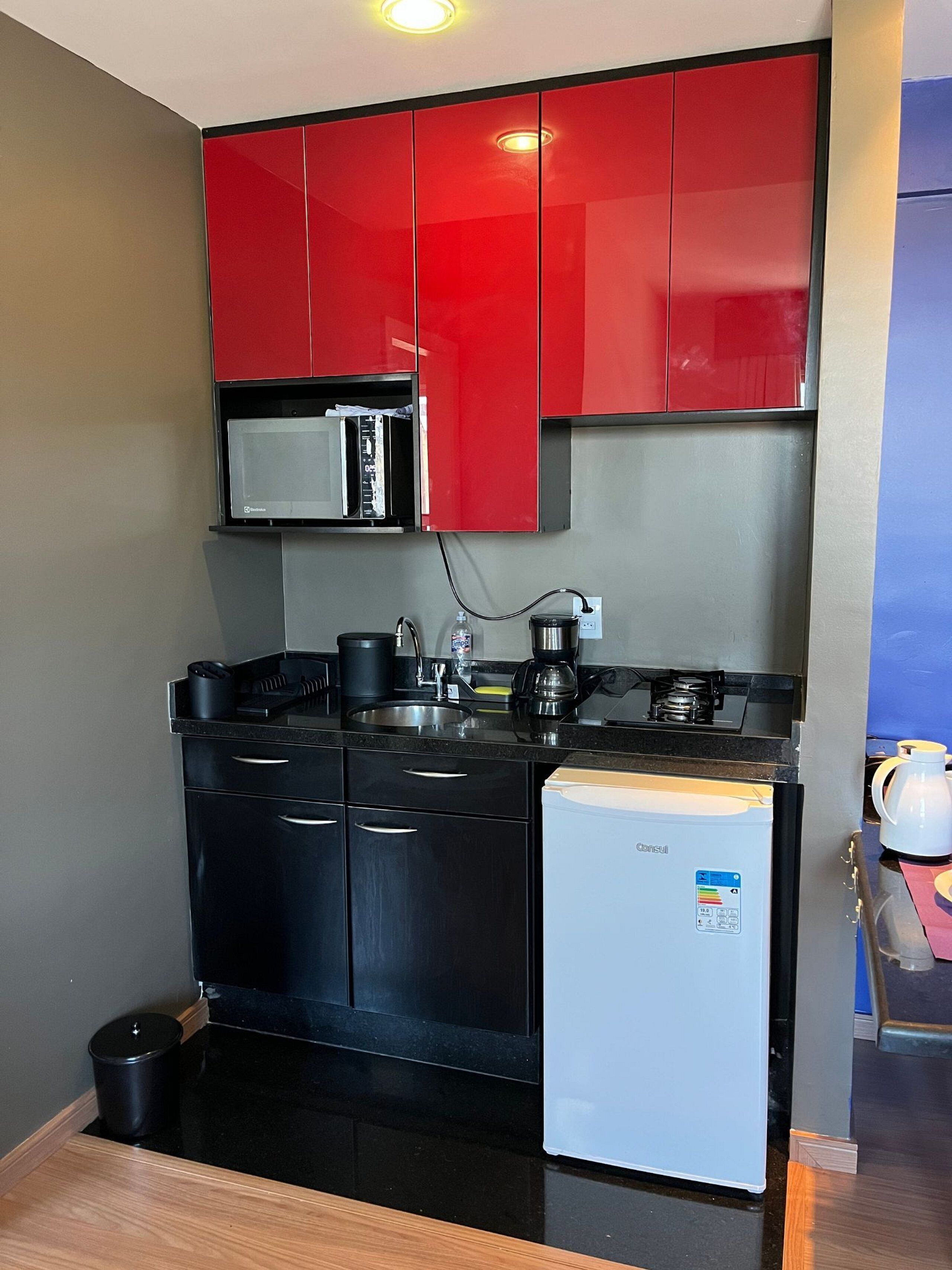 Uma cozinha compacta com eletrodomésticos pretos, uma geladeira branca e armários vermelhos.