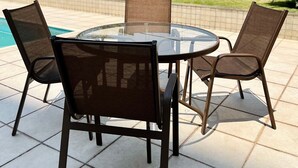 An outdoor patio with a round glass table and four chairs, a swimming pool, and a cityscape in the background. - LK Barro Preto 5 (Belo Horizonte)