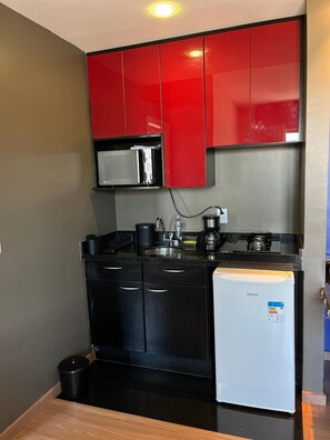 A compact kitchen with black cabinets, a white refrigerator, a microwave, and a coffee maker. - LK Barro Preto 5 (Belo Horizonte)
