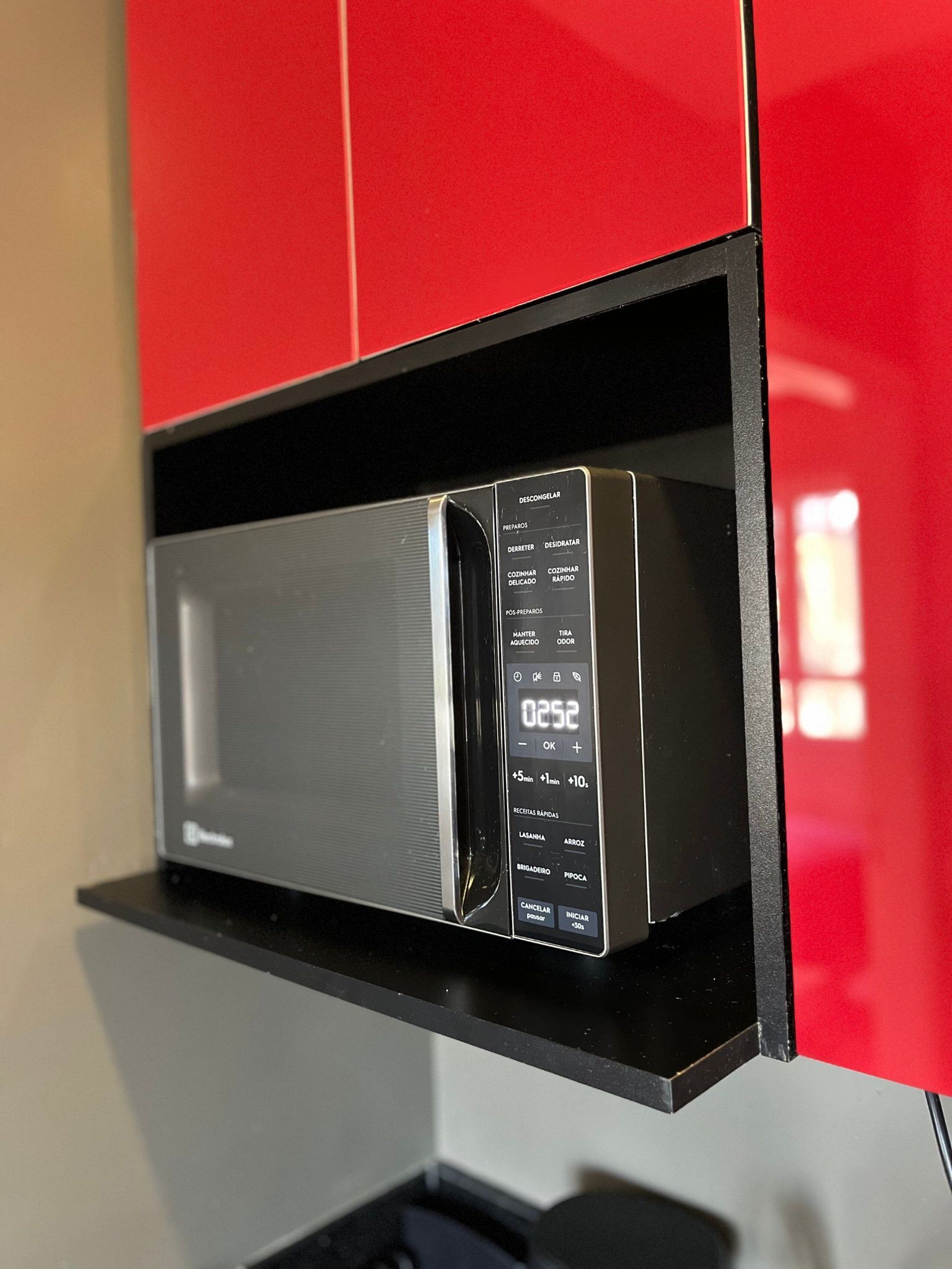 A microwave with a digital display, set in a kitchen with red cabinets.