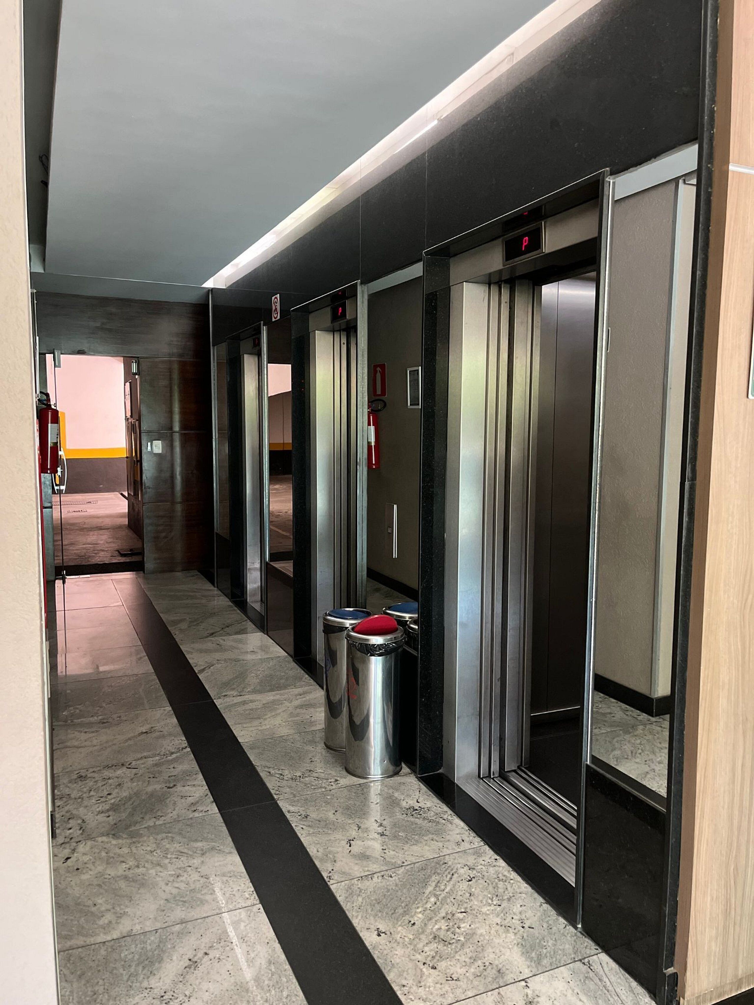 A hallway with elevators, a trash bin, and a fire extinguisher.