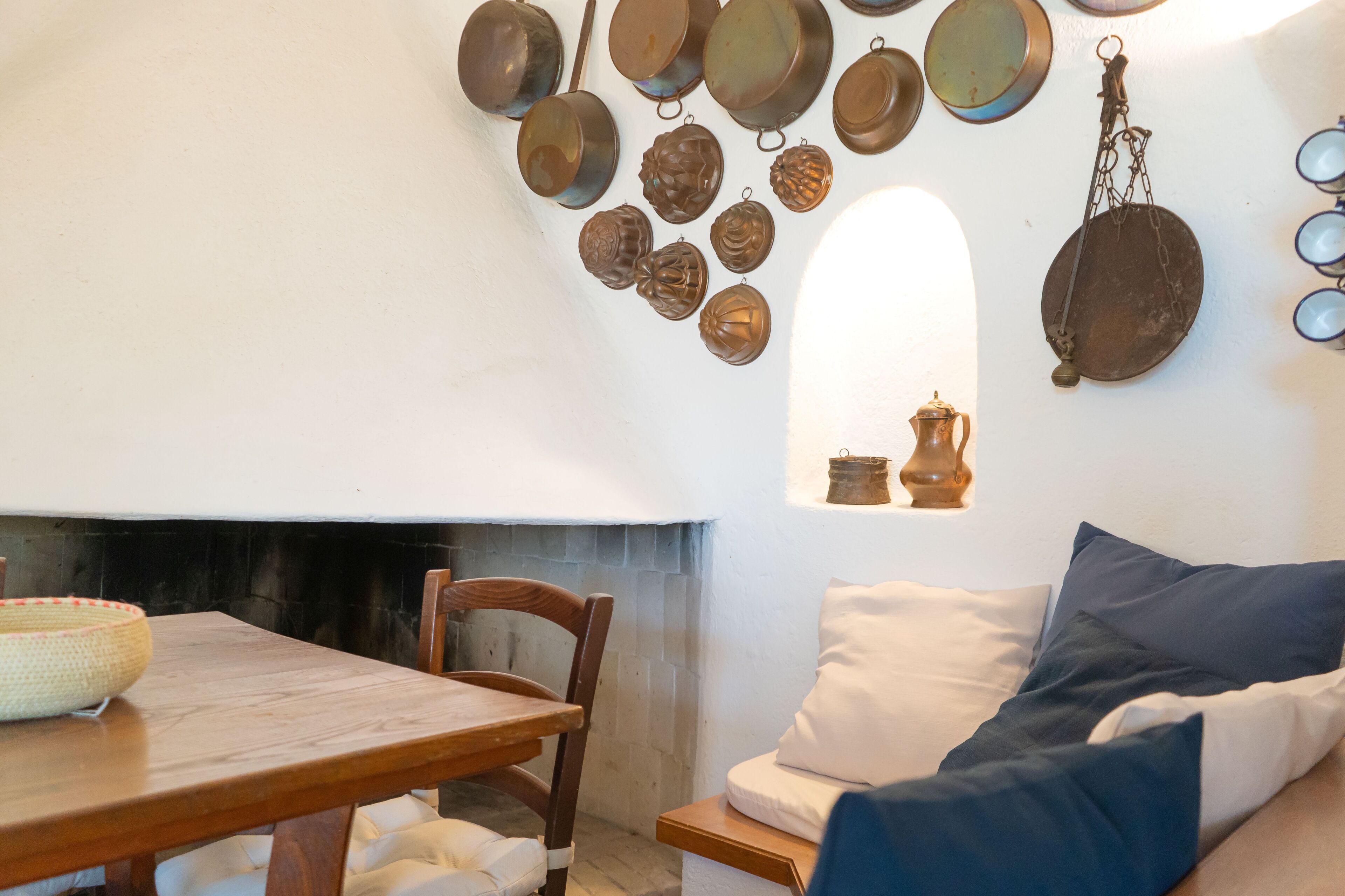 A dining area with a wooden table and chairs, a sofa with cushions, and a wall adorned with various metal kitchen items.