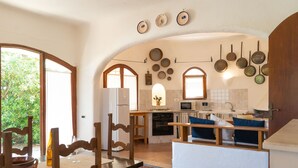 Een keuken met een kookeiland, houten stoelen, een eettafel en uitzicht op groen buiten.