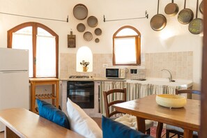 Eine Küche mit Essbereich, einem Kühlschrank, einer Mikrowelle, einem Spülbecken und einem Fenster mit Vorhängen.