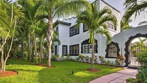 A white building with black window frames and a stone facade, surrounded by a well-maintained lawn and palm trees. - 5 Bedroom Mini Resort with Pool! (Boynton Beach)