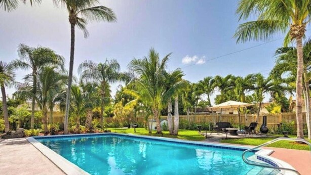A swimming pool surrounded by palm trees and a wooden fence. - 5 Bedroom Mini Resort with Pool! (Boynton Beach)