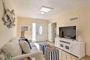 Een woonkamer met een bank, poefjes, een televisie en een kast.