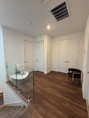 Een ruime kamer met houten vloer, witte wanden en een glazen balustrade met uitzicht op een lager gelegen niveau.