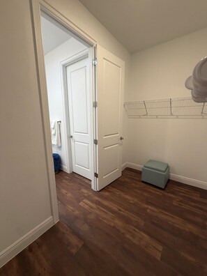Ett rum med trägolv, en vit dörr, en blå bänk och ett metallställ för torkning av kläder på väggen.