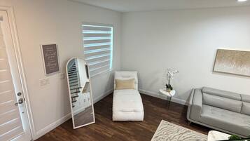 Un salon moderne avec un canapé, une petite table sur laquelle est posée une plante, un miroir et un lit avec une tête de lit.