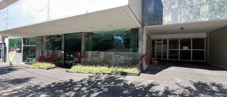 A modern building with a covered entrance, large windows, and a paved area with planters.