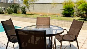 Een ronde glazen tafel met vier stoelen, omgeven door een betegeld terras met uitzicht op een stadslandschap.