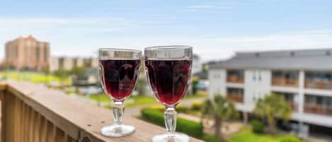 Two wine glasses on a balcony with a view of buildings and greenery.