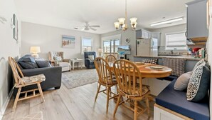Uma sala de estar moderna com sofá, mesa de jantar com cadeiras, área de cozinha e ventilador de teto.