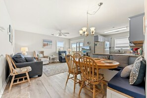 A modern living room with a sofa, a dining table with chairs, a kitchen area, and a ceiling fan. - Ocean Terrace I A2 - Cherry Grove Condo (North Myrtle Beach)