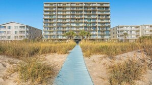 Et hotel ved stranden med flere etager, en midtersti og frodig beplantning omkring.