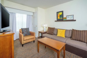 Una habitación de hotel con televisión, sofá, sillón, mesa de centro y lámpara.